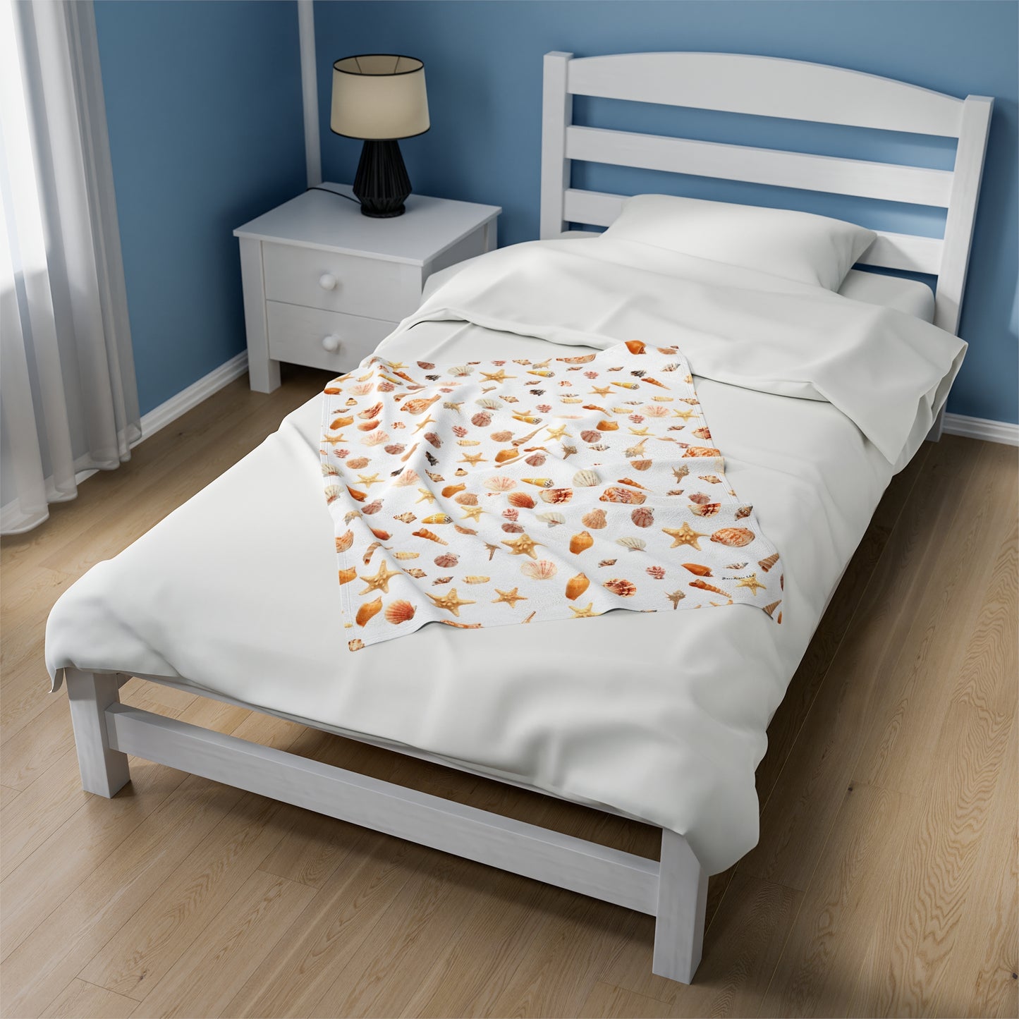Sea shell velveteen blanket displayed on a bed with white sheets and a cozy bedroom setting
